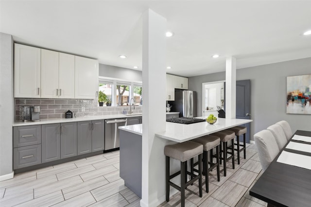 2222 Ravenwood Dr, Grand Prairie, TX 75050 - kitchen featuring appliances with stainless steel finishes, a kitchen breakfast bar, a sink, light countertops, and decorative backsplash