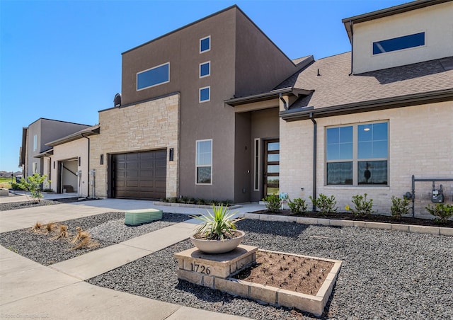 modern home with roof with shingles, stone siding, concrete driveway, an attached garage, and stucco siding