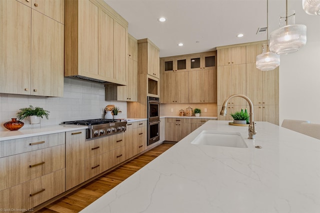 kitchen featuring light stone countertops, stainless steel appliances, light brown cabinetry, and a sink