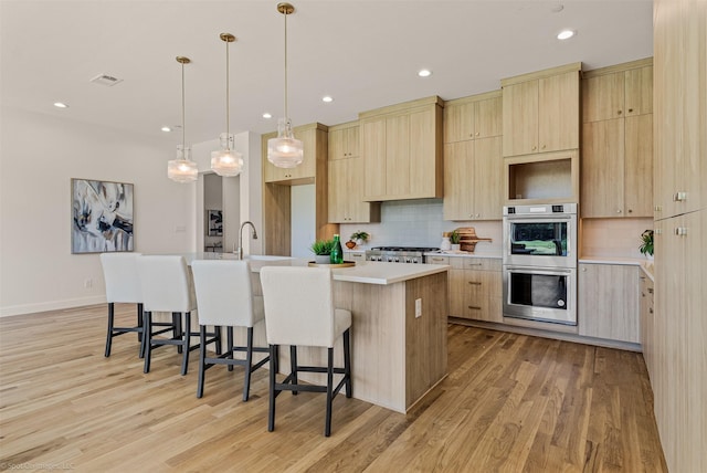 kitchen featuring light wood-type flooring, a kitchen island with sink, light brown cabinets, and double oven
