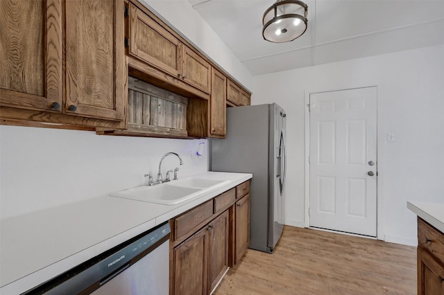 kitchen with a sink, brown cabinets, light wood finished floors, light countertops, and appliances with stainless steel finishes