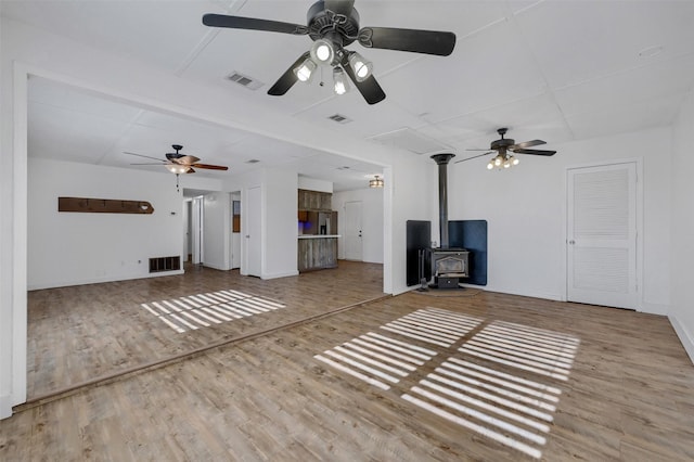 unfurnished living room with a wood stove, visible vents, and ceiling fan