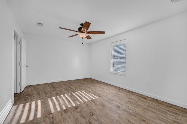 empty room with wood finished floors, visible vents, a ceiling fan, and baseboards