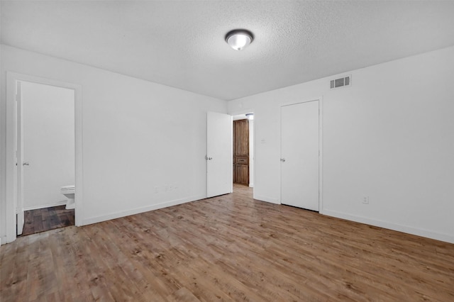 unfurnished bedroom with wood finished floors, a textured ceiling, ensuite bath, baseboards, and visible vents