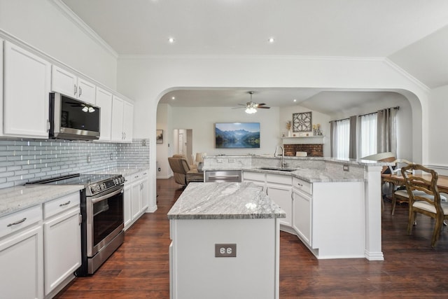 kitchen with appliances with stainless steel finishes, arched walkways, a center island with sink, a sink, and open floor plan