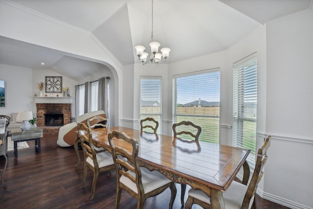 dining room with a brick fireplace, wood finished floors, arched walkways, a notable chandelier, and vaulted ceiling