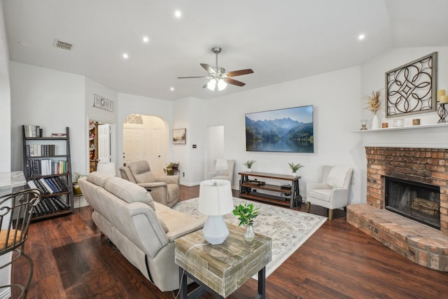 living room featuring a ceiling fan, visible vents, arched walkways, a brick fireplace, and wood finished floors