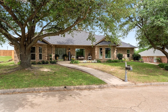 single story home featuring a shingled roof, a front lawn, and brick siding