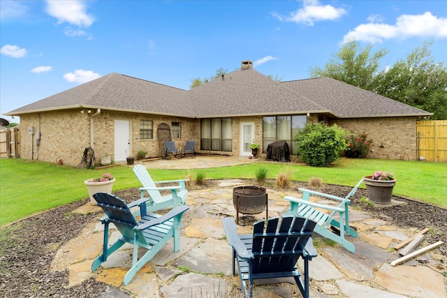 rear view of property featuring roof with shingles, brick siding, fence, a patio, and a fire pit