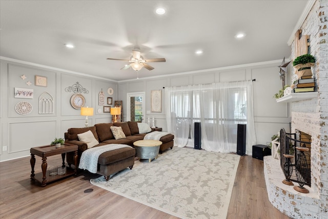 living room featuring crown molding, ceiling fan, a decorative wall, a brick fireplace, and wood finished floors