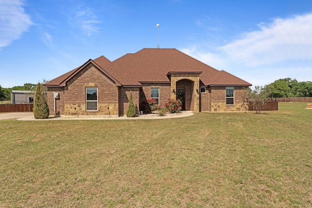 ranch-style home with fence, a front lawn, brick siding, and roof with shingles