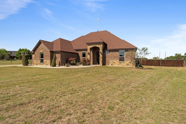 view of front of property featuring brick siding, a front lawn, fence, and roof with shingles