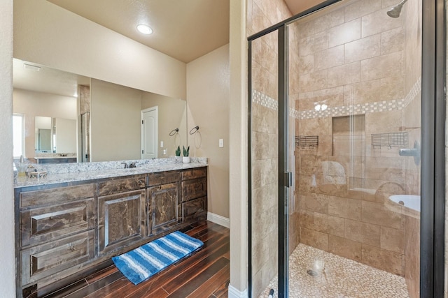 full bath with baseboards, wood finished floors, double vanity, and a stall shower