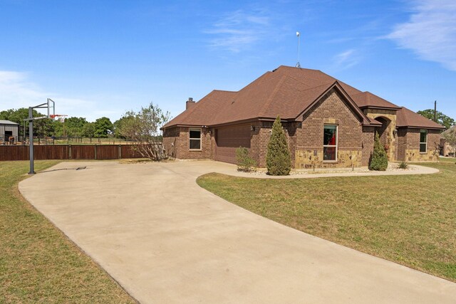 exterior space featuring a chimney, concrete driveway, fence, brick siding, and a lawn