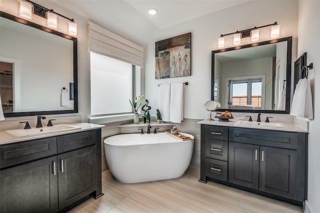 full bath with two vanities, a sink, recessed lighting, and a freestanding bath