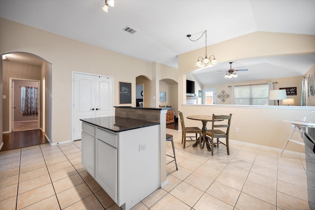 kitchen with light tile patterned flooring, dark countertops, visible vents, a ceiling fan, and a kitchen island