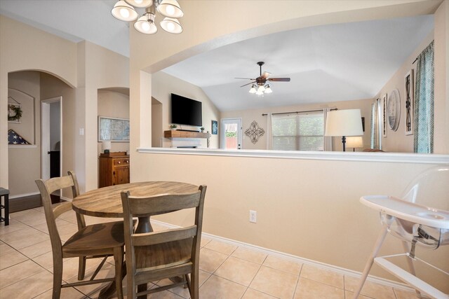 dining space with ceiling fan with notable chandelier, light tile patterned floors, arched walkways, baseboards, and lofted ceiling