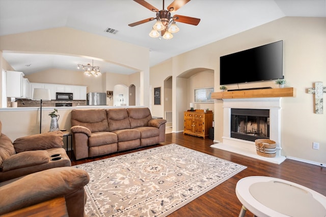 living area featuring vaulted ceiling, dark wood-style flooring, a fireplace with raised hearth, and ceiling fan with notable chandelier