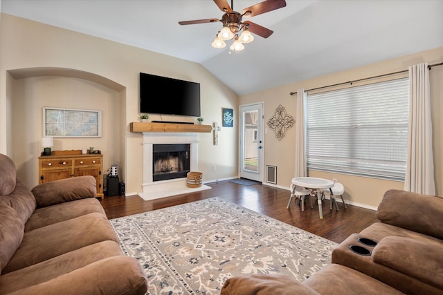 living room featuring lofted ceiling, a fireplace with raised hearth, wood finished floors, baseboards, and ceiling fan