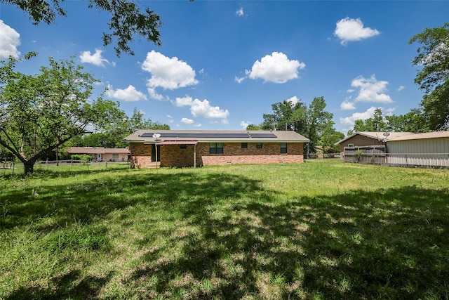 back of property featuring roof mounted solar panels, fence, a yard, and brick siding