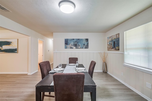 dining room featuring light wood finished floors, visible vents, baseboards, wainscoting, and a textured ceiling