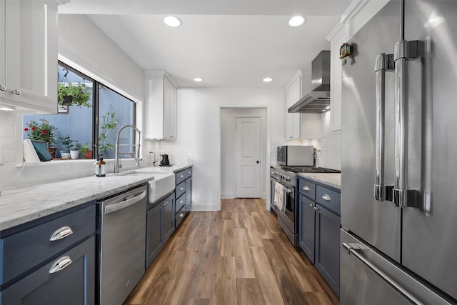 kitchen with white cabinets, high end appliances, light stone counters, wood finished floors, and wall chimney exhaust hood
