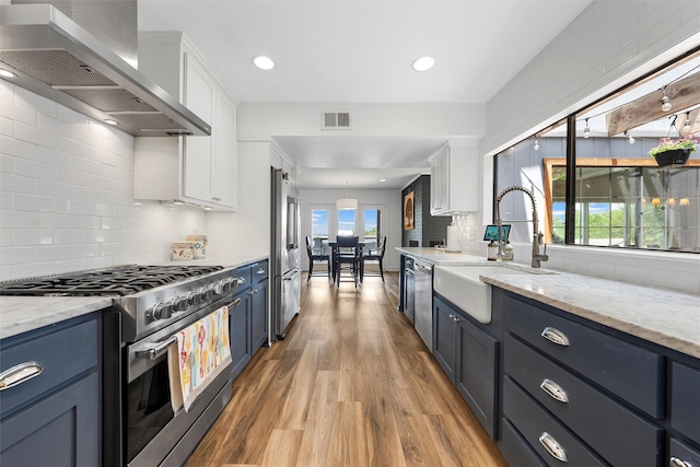 kitchen featuring wall chimney range hood, wood finished floors, premium appliances, a sink, and visible vents