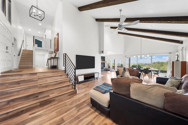 living area with high vaulted ceiling, stairway, ceiling fan with notable chandelier, light wood finished floors, and beam ceiling