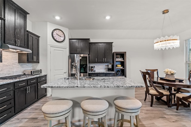 kitchen with light stone countertops, decorative backsplash, under cabinet range hood, and stainless steel appliances