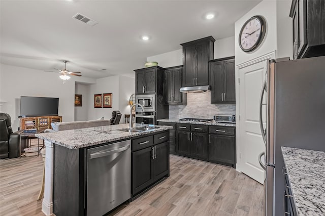 kitchen with open floor plan, under cabinet range hood, appliances with stainless steel finishes, and dark cabinets