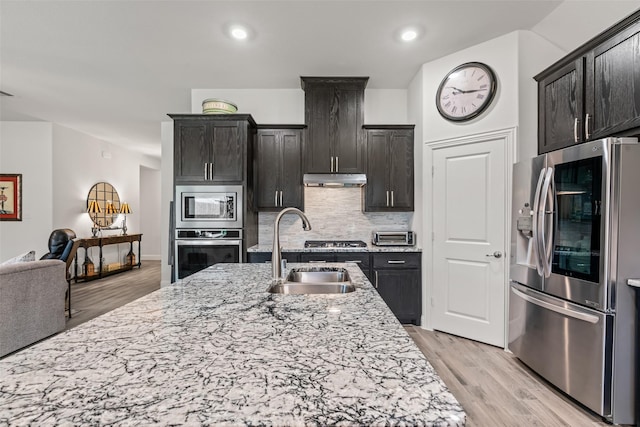 kitchen featuring stainless steel appliances, a sink, backsplash, and light stone counters