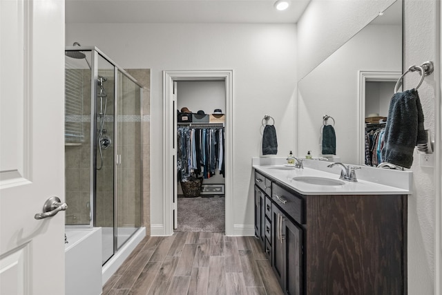 bathroom with wood finished floors, a sink, double vanity, and a stall shower