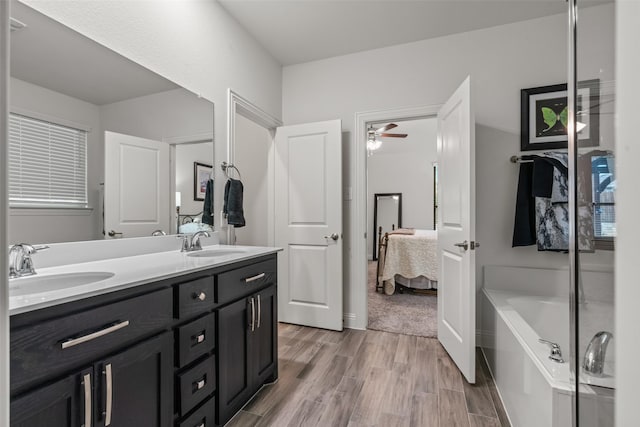 ensuite bathroom featuring a garden tub, ensuite bath, wood finished floors, and a sink