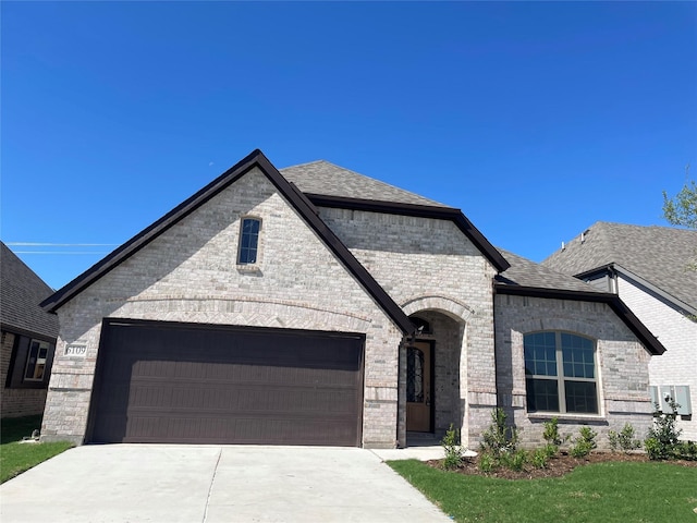 6109 Rodin Dr, Royse City, TX 75189 - french country home featuring concrete driveway, an attached garage, brick siding, and a shingled roof