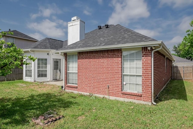 rear view of house with brick siding, a yard, a chimney, and fence