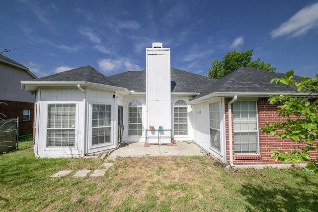 back of house featuring roof with shingles, a chimney, brick siding, a patio area, and a yard
