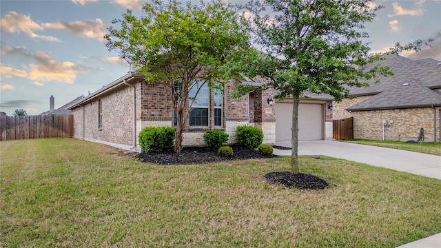 view of front facade featuring driveway, fence, brick siding, an attached garage, and a yard