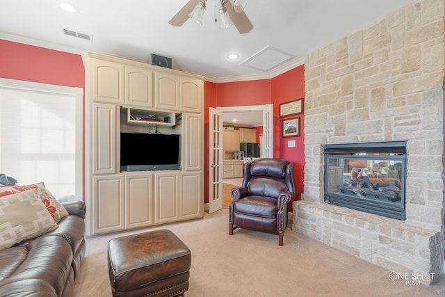 living room featuring visible vents, light colored carpet, a ceiling fan, a stone fireplace, and ornamental molding