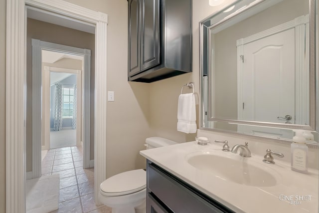 half bathroom featuring stone tile flooring, baseboards, toilet, and vanity