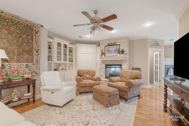 living room with visible vents, a ceiling fan, light wood-style floors, crown molding, and a fireplace