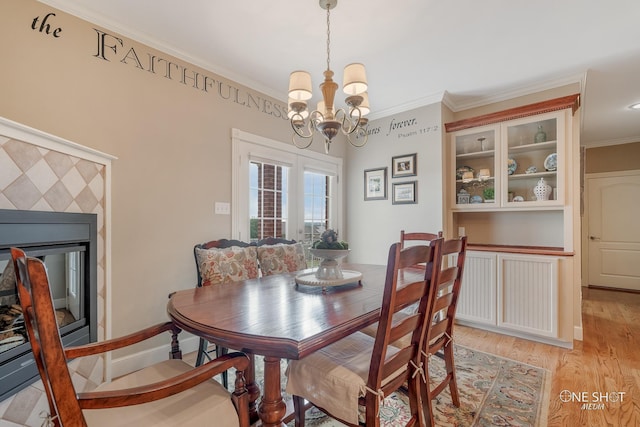 dining area featuring a glass covered fireplace, light wood-style floors, a notable chandelier, and ornamental molding