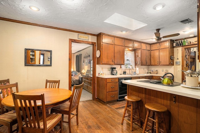 kitchen featuring a skylight, brown cabinets, dark wood finished floors, light countertops, and black appliances