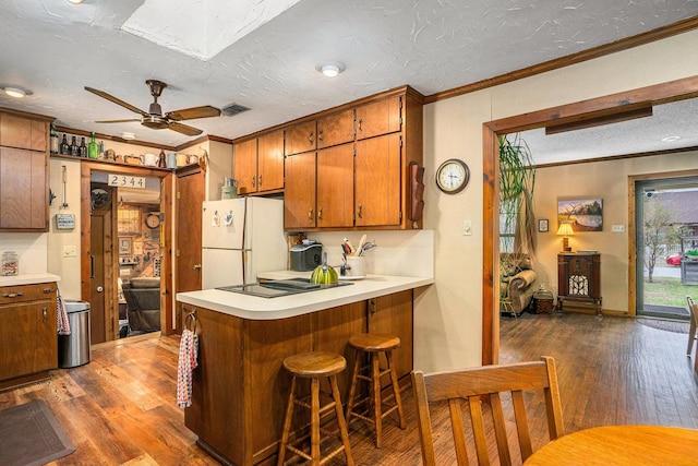 kitchen with crown molding, brown cabinets, ceiling fan, dark wood-style flooring, and freestanding refrigerator