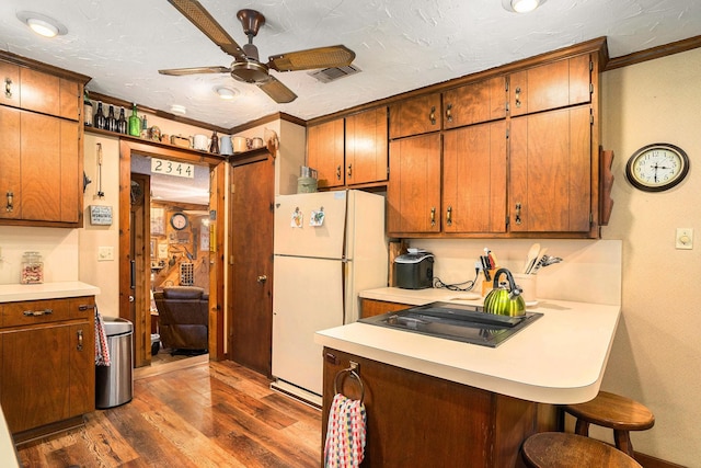 kitchen with freestanding refrigerator, a kitchen breakfast bar, dark wood-style floors, light countertops, and a ceiling fan