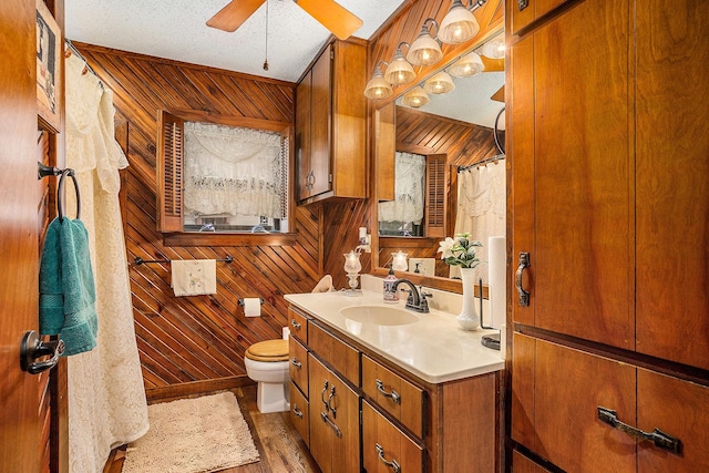bathroom with vanity, wood walls, wood finished floors, toilet, and ceiling fan