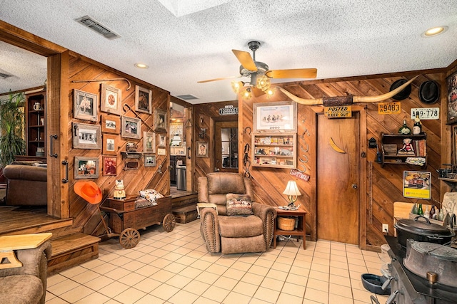 sitting room with ceiling fan, a textured ceiling, wood walls, light tile patterned floors, and visible vents