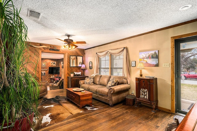 living room with visible vents, ornamental molding, ceiling fan, wooden walls, and hardwood / wood-style flooring
