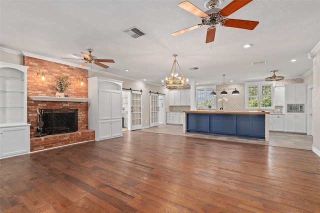 unfurnished living room with hardwood / wood-style flooring, ornamental molding, ceiling fan, and a barn door