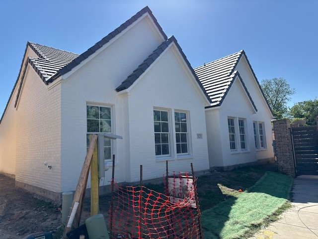 back of property with a tile roof, brick siding, and fence