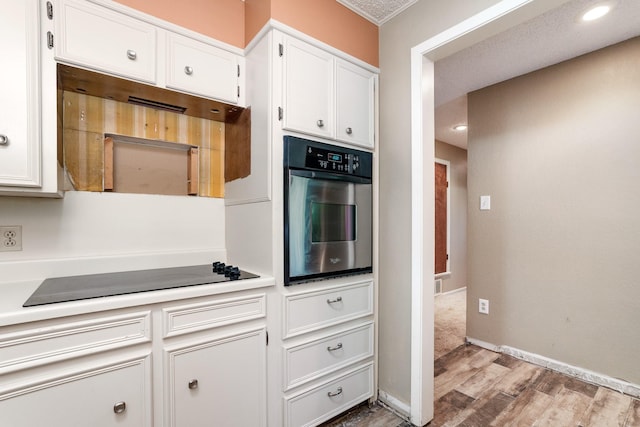 kitchen with white cabinets, light wood finished floors, stainless steel oven, black electric stovetop, and light countertops
